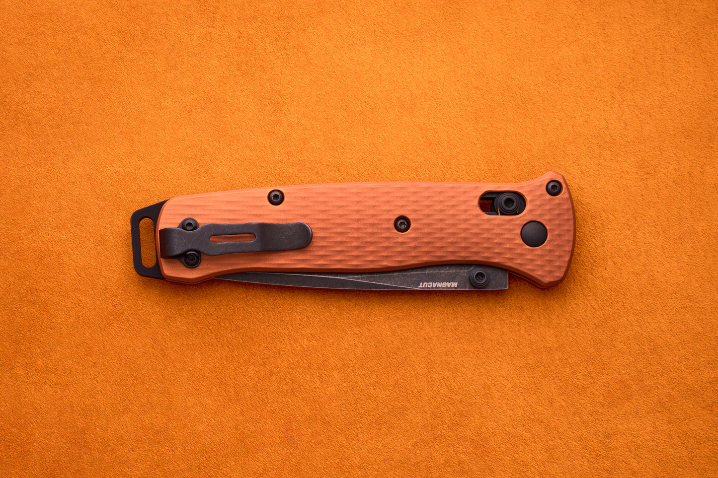 A folded Benchmade Bailout with an orange handle, textured grip, and black clip is set on an orange surface, highlighting its ultralight design ideal for everyday carry.
