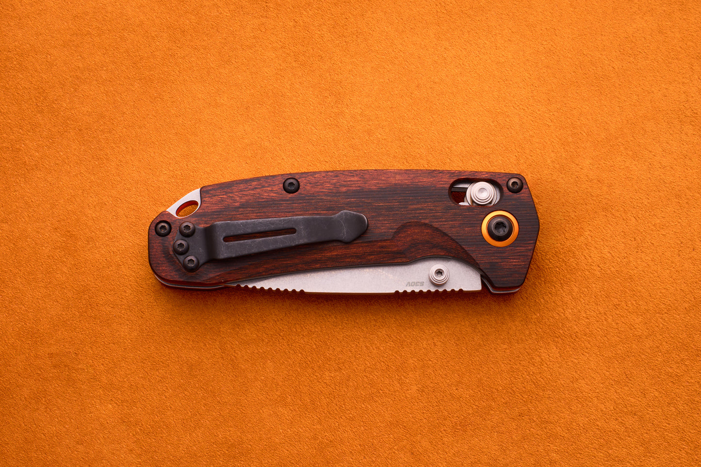 A Benchmade North Fork folding pocket knife with a wooden handle and a partially visible CPM-S30V blade lies closed on an orange suede surface.