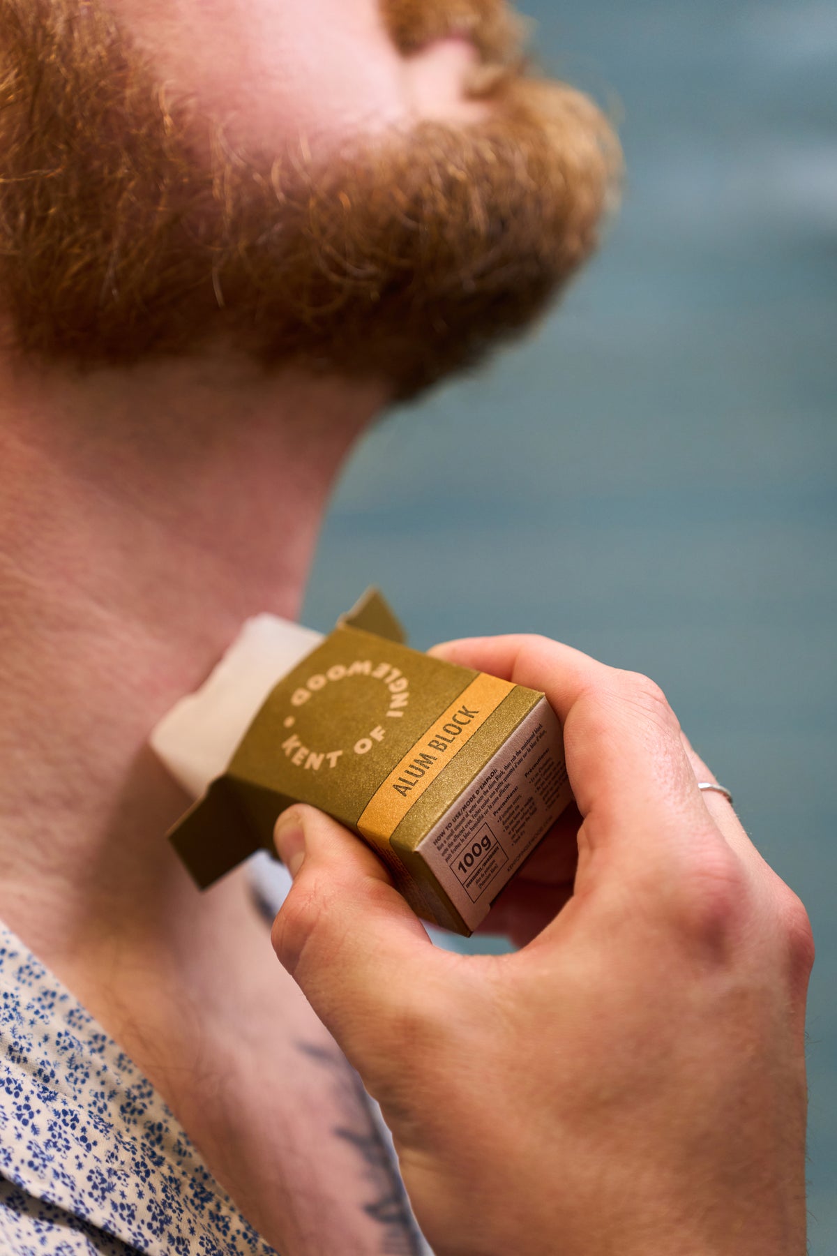 After shaving, a person uses the Kent of Inglewood Potassium Alum Block on their neck, holding the block in one hand to help stop bleeding from minor nicks, while their face tilts upward for a close-up view of the application.