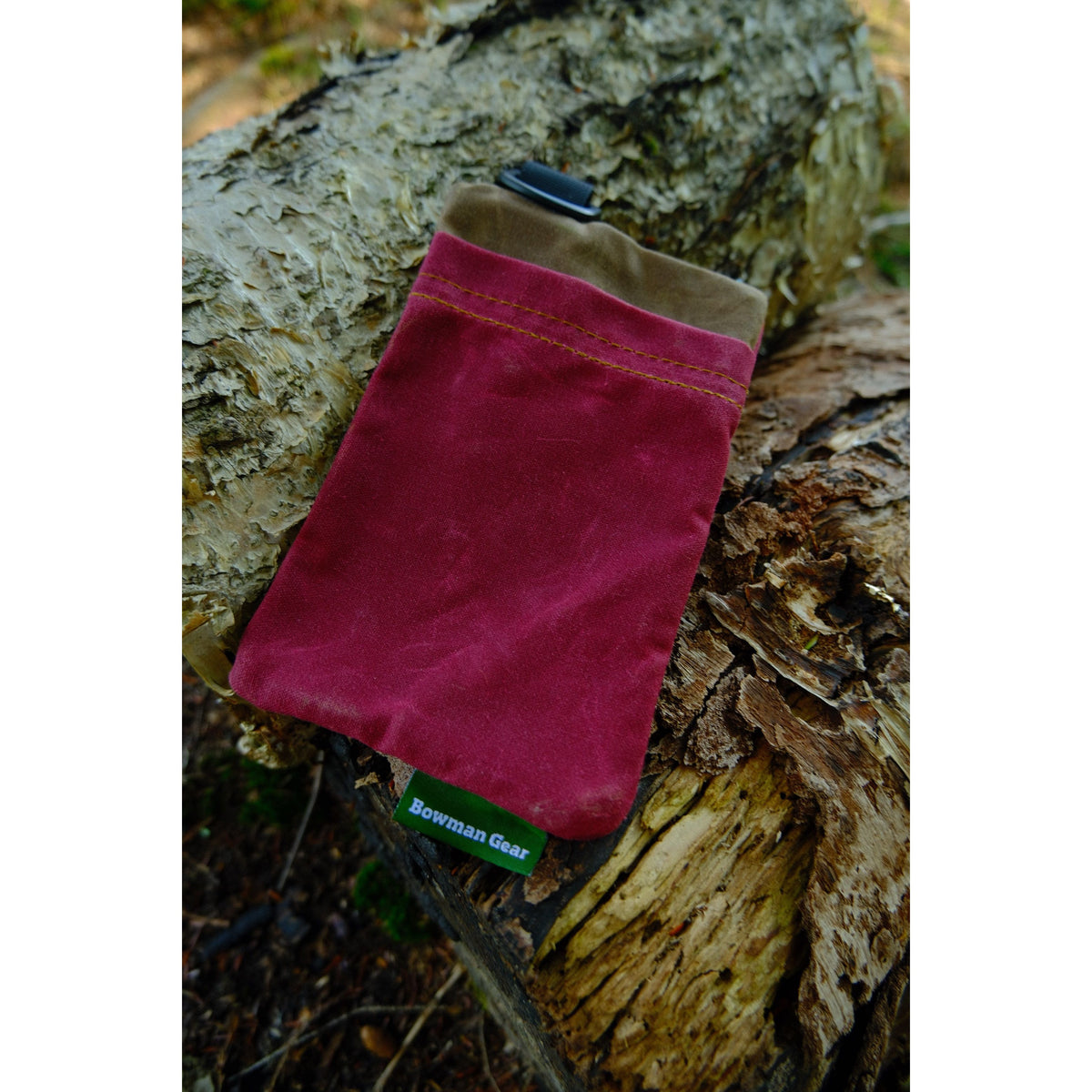 A red and brown Bowman Gear Sentry Waxed Canvas EDC Pouch sits atop a weathered tree log outdoors, providing rugged storage for essential items on any adventure.