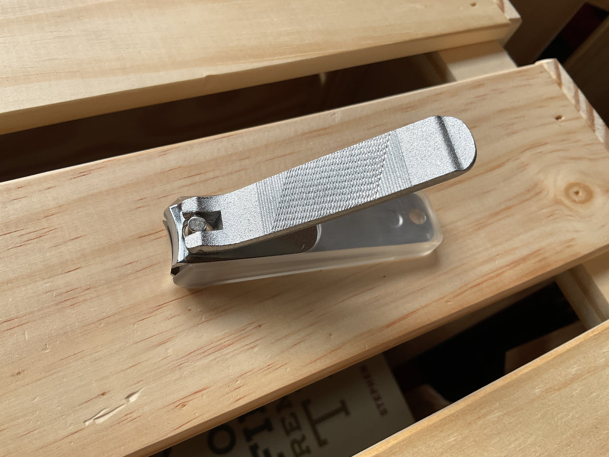 A silver metal Touroku Sakai Nail Clipper with a textured lever resting on a wooden crate.