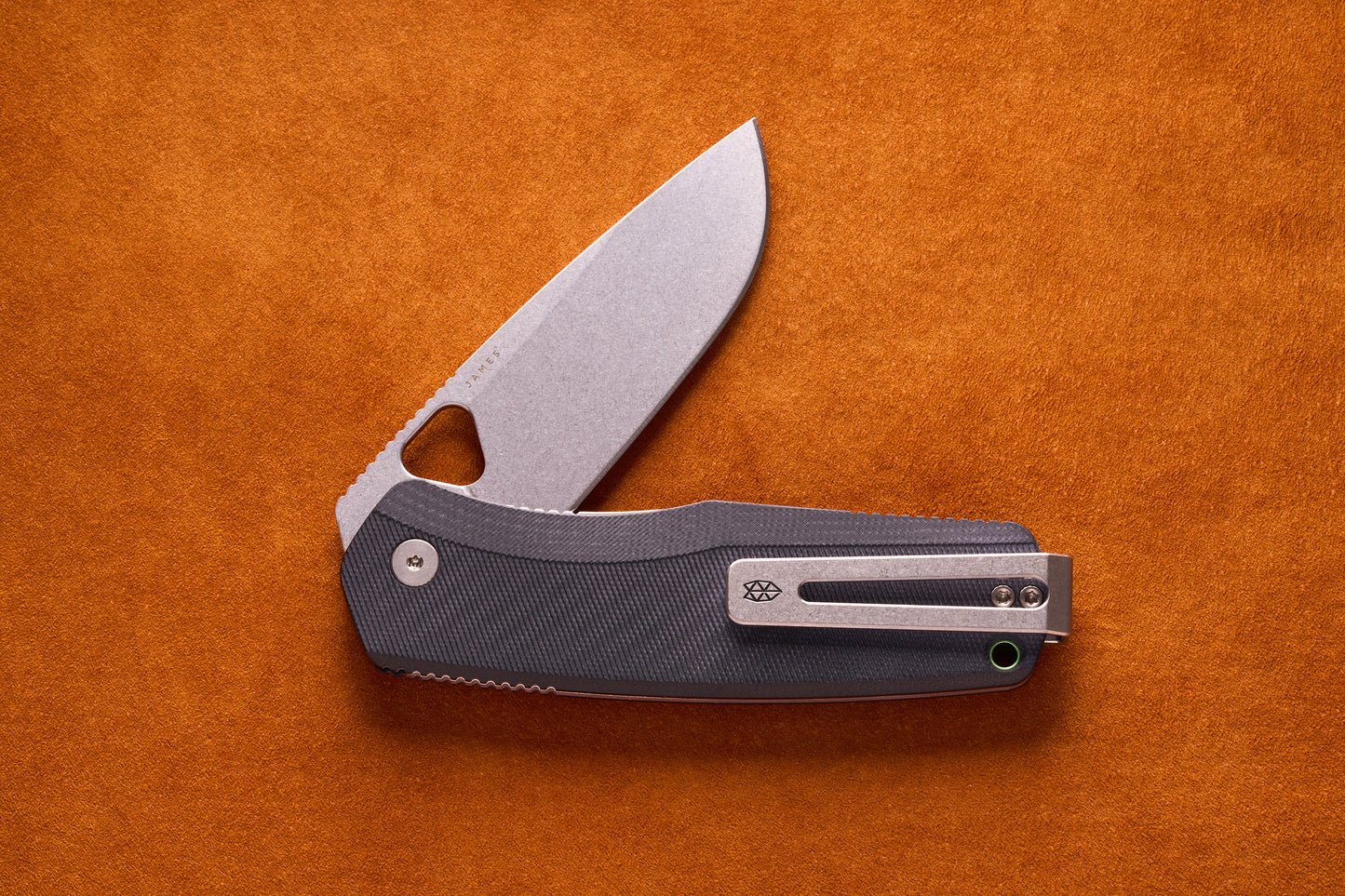 James Folsom Pro folding pocket knife with stonewashed drop-point blade, triangular thumb-hole, dark handle, and titanium pocket clip, displayed on a suede-like surface.