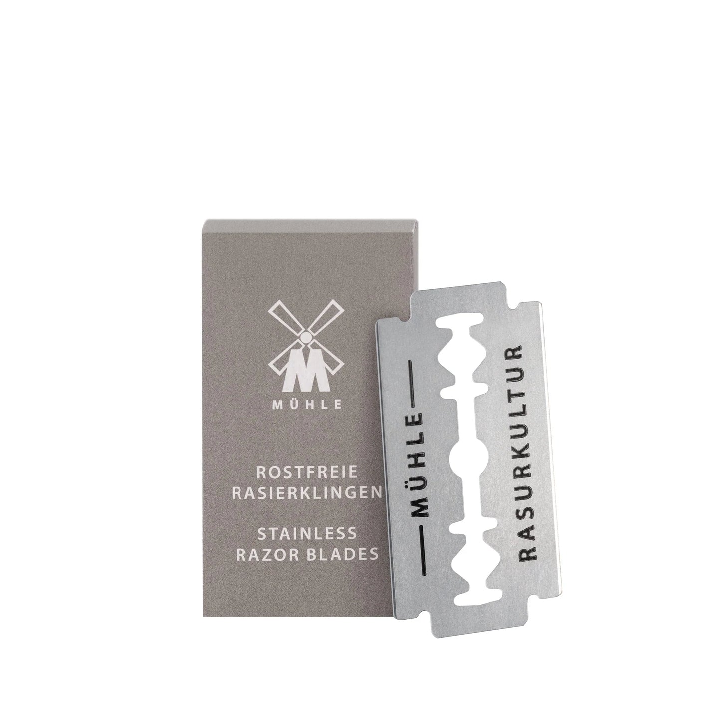 A box of Mühle Safety Razor Blades stands upright next to a single double-edged blade, both showcasing the brand’s minimalist design.