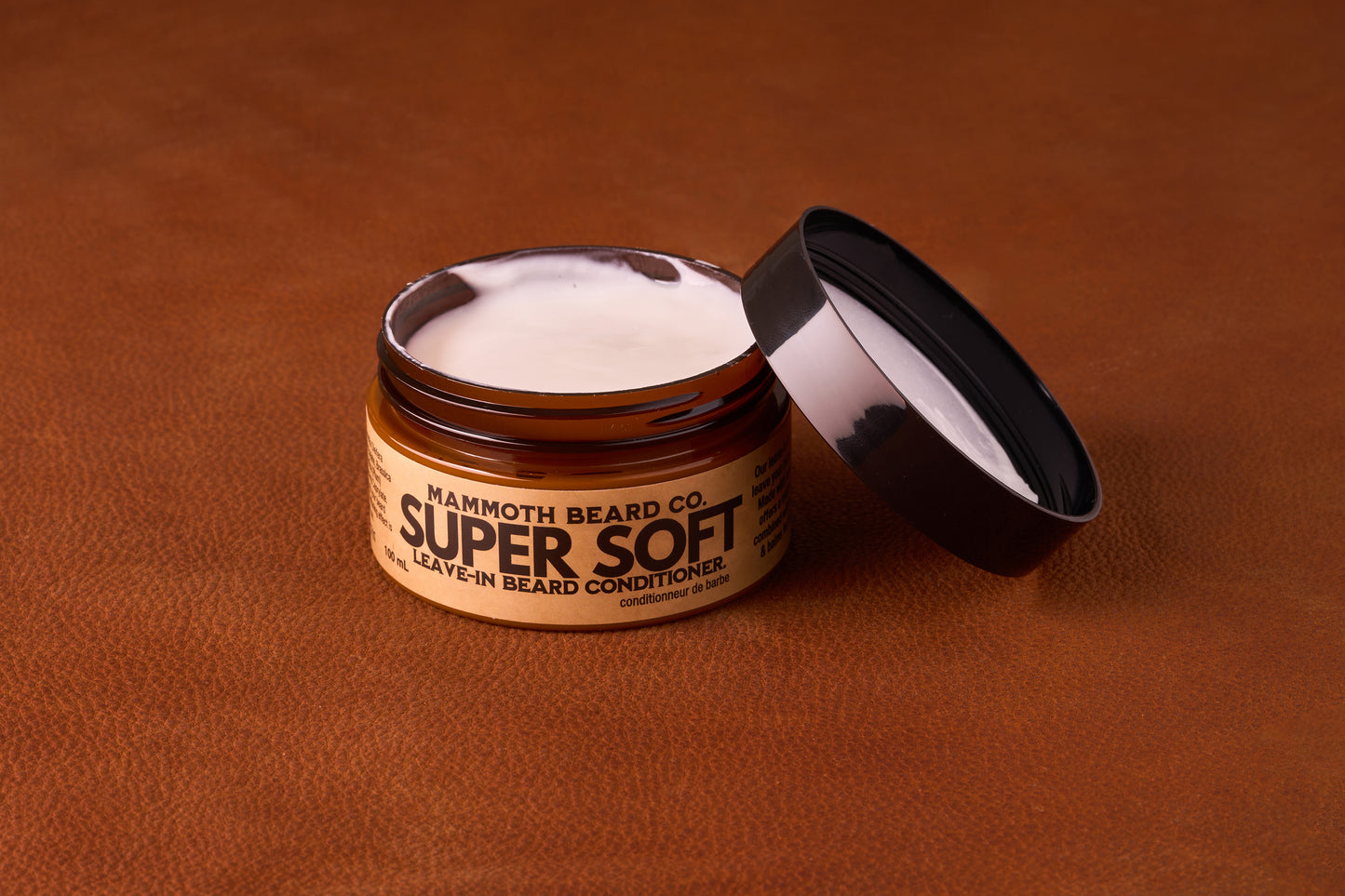 Mammoth Beard Co. Super Soft Leave-In Beard Conditioner Cream Unscented 100ml in an open amber jar, showcasing its creamy texture on a leather-like surface.