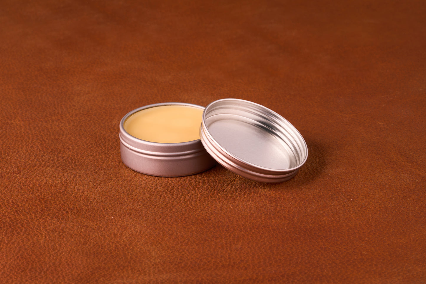 Mammoth Beard Co. Unscented Moustache Wax in an open metal tin showcasing smooth, pale yellow balm on a brown textured surface, ideal for versatile styling.
