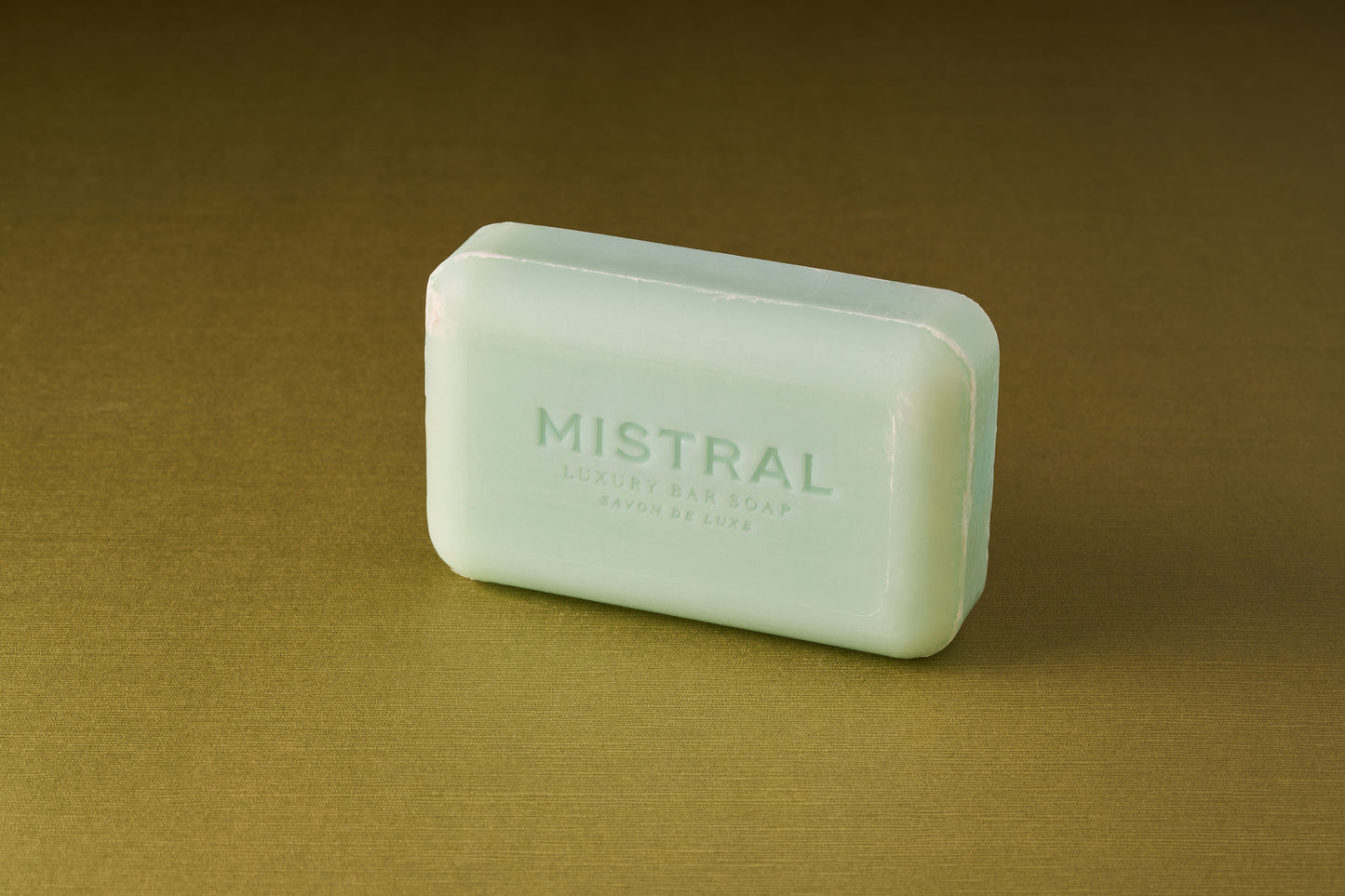 A rectangular, light green Mistral Marbles Marine Bar Soap rests on a plain olive surface, exuding a refined French-inspired fragrance.