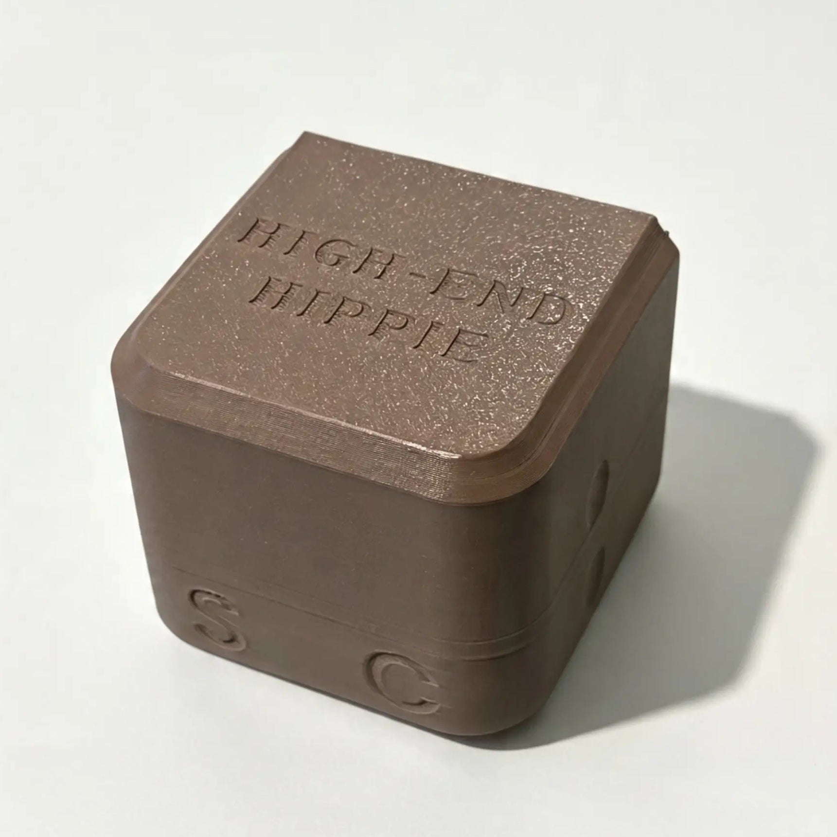 A brown, cube-shaped case with “HIGH END HIPPIE” engraved on the top and the letters S and C on its sides, designed specifically for The High End Hippie 2-in-1 Shampoo and Conditioner—perfect for sustainable shower storage, shown resting on a plain white surface.