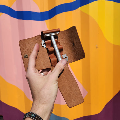 Jack Raymond Leather Safety Razor Holster held open, displaying a metal safety razor with an aluminum handle and two loose blades, designed for travel grooming.