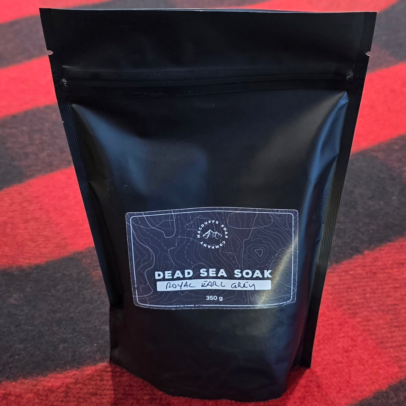 A black bag of bath salts on a red plaid background