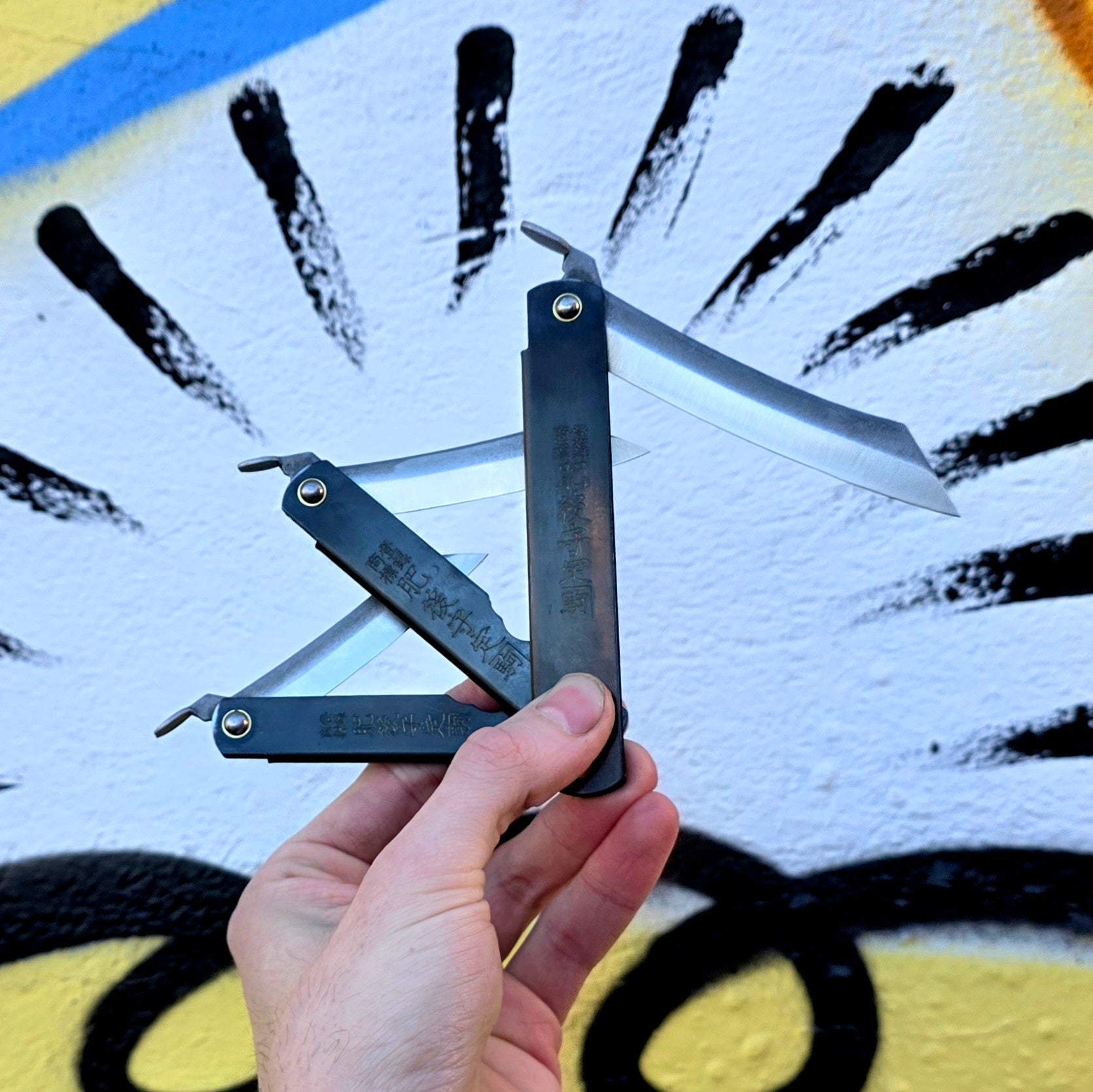 Hand holding a folding knife against a graffiti-covered wall