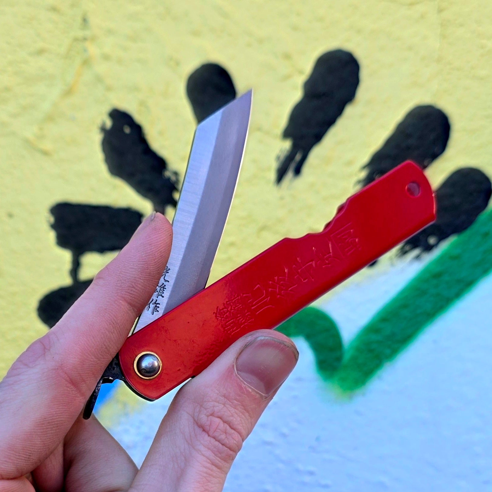 Red pocket knife with a blurred background featuring cacti