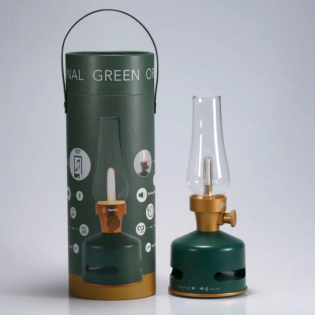 The KooKoo MoriMori Light & Sound Lantern, featuring a green and gold vintage-inspired design, stands next to its matching cylindrical packaging; the packaging presents product images and information on a gray background, emphasizing the lantern’s nostalgic aesthetic.