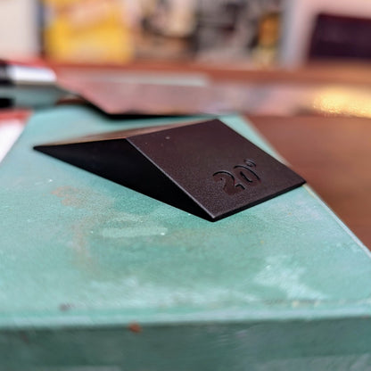 Knifewear Sharpening Angle Guide on a workbench, showing its wedge design with a 20° marking, ideal for precise blade sharpening and tool angle setting.