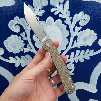 Kershaw Federalist knife with a satin drop-point blade and textured canvas-micarta handle, showcasing traditional craftsmanship and ergonomic design, held in a hand.