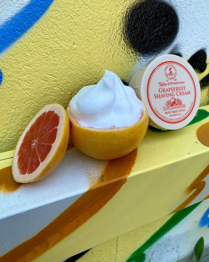 Grapefruit shaving cream in a halved grapefruit with a branded container on a colorful background