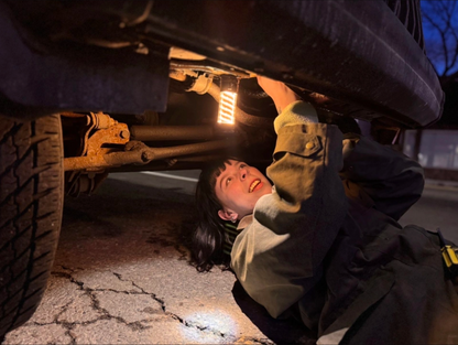 Person using Barebones Edison Light Stick to inspect undercarriage of vehicle at night, highlighting its utility as an emergency flashlight and outdoor lantern.