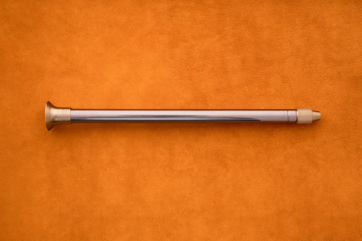The Barebones Telescoping Fire Blower rests horizontally on an orange suede surface, evoking the must-have tools you’d bring along for an outdoor adventure.