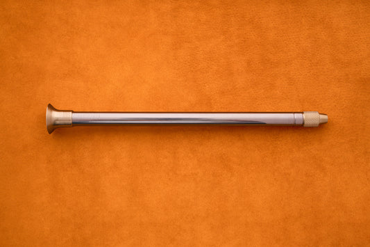 The Barebones Telescoping Fire Blower rests horizontally on an orange suede surface, evoking the must-have tools you’d bring along for an outdoor adventure.