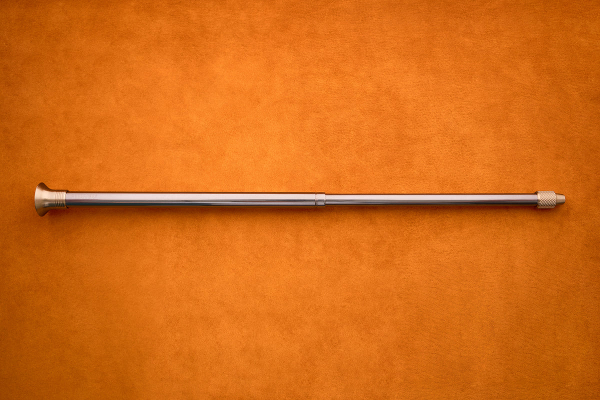 The Barebones Telescoping Fire Blower, featuring a flared end and screw tip, is shown lying horizontally on an orange textured surface—perfectly poised to enhance your next outdoor campfire experience.