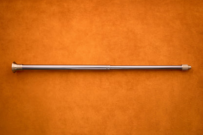 The Barebones Telescoping Fire Blower, featuring a flared end and screw tip, is shown lying horizontally on an orange textured surface—perfectly poised to enhance your next outdoor campfire experience.