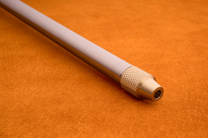 A close-up of the Barebones Telescoping Fire Blower—a metallic cylindrical tool with a textured grip—resting on an orange suede surface. This essential accessory is designed to enhance any campfire and elevate your outdoor experience.