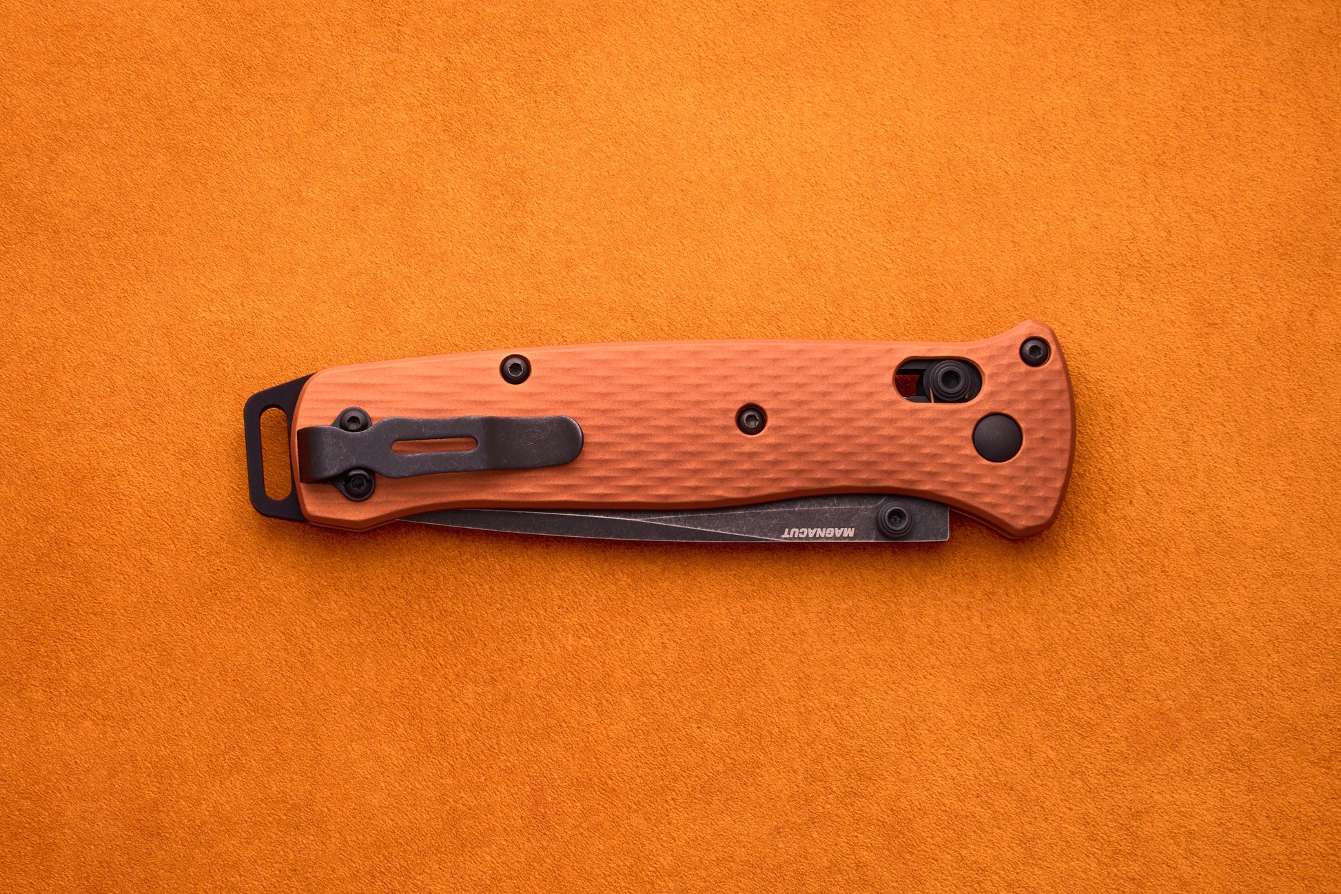 A folded Benchmade Bailout with an orange handle, textured grip, and black clip is set on an orange surface, highlighting its ultralight design ideal for everyday carry.