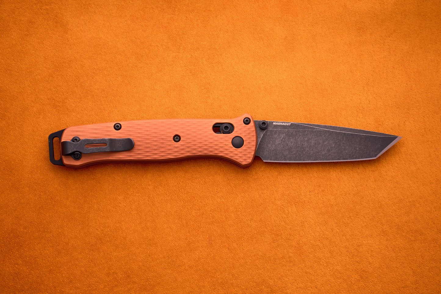 A Benchmade Bailout featuring a textured orange handle and a dark tanto-style CPM-Magnacut blade, inspired by ultralight design, shown on an orange background.