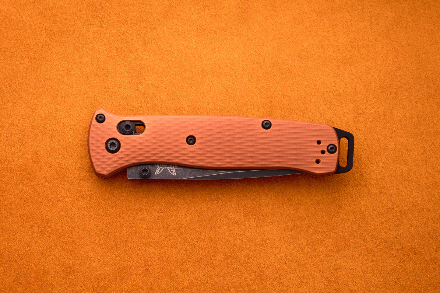 A closed Benchmade Bailout folding pocket knife with an orange textured handle rests on an orange surface, highlighting its ultralight design and the durability of its CPM-Magnacut blade.