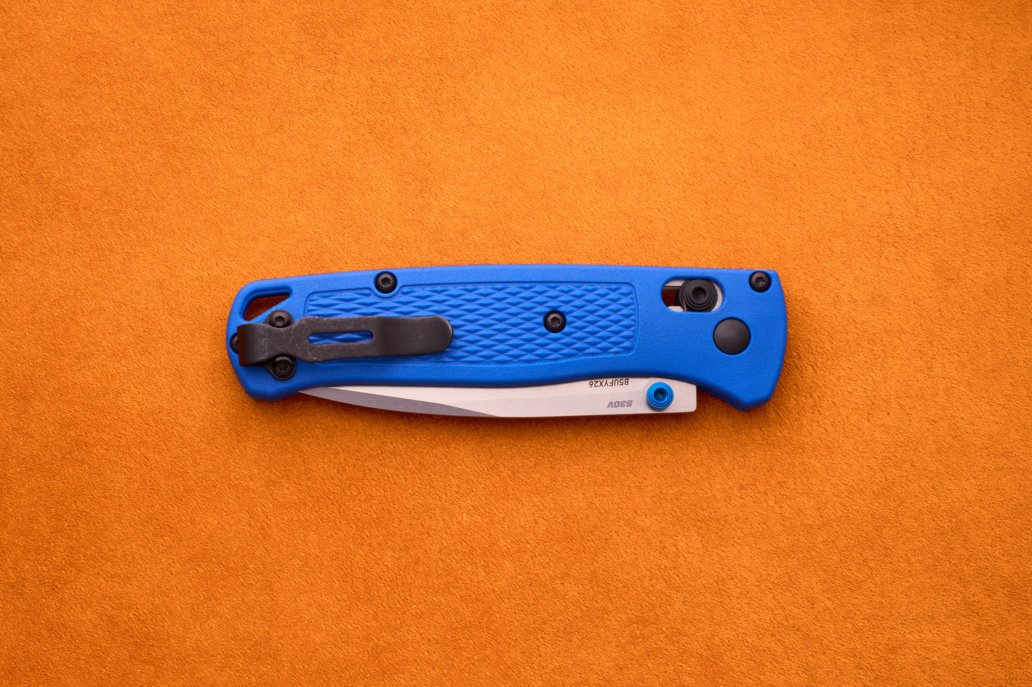A Benchmade Bugout with a blue handle and a partially exposed S30V stainless steel blade rests on an orange textured surface, ready for your next outdoor adventure.