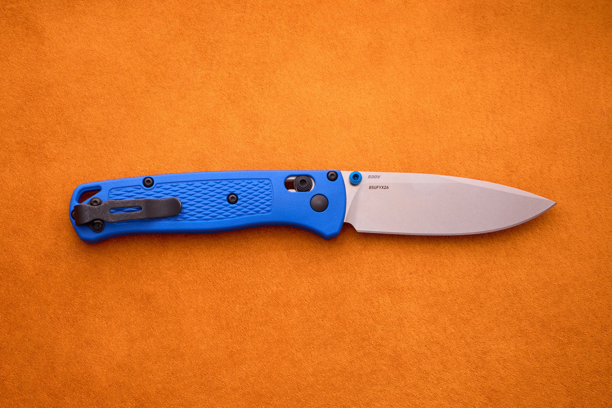A Benchmade Bugout with a blue textured handle and a silver blade rests open on an orange background, perfect for your next outdoor adventure.