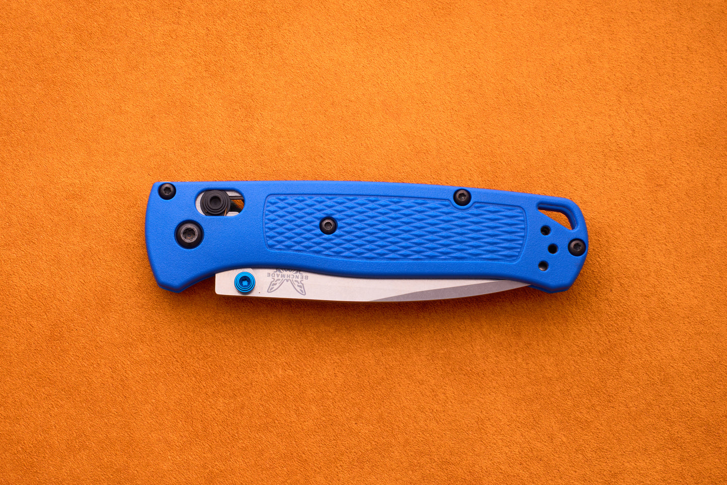 A closed Benchmade Bugout with a blue textured handle and a partially visible silver blade rests on an orange surface, making the Benchmade Bugout an excellent companion for any outdoor adventure.