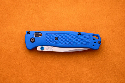 A closed Benchmade Bugout with a blue textured handle and a partially visible silver blade rests on an orange surface, making the Benchmade Bugout an excellent companion for any outdoor adventure.
