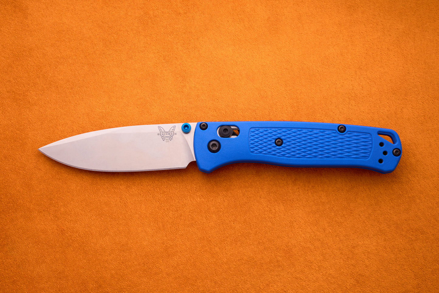 The Benchmade Bugout, featuring an S30V stainless steel silver blade and a textured blue handle, is shown open against an orange background, making it the ideal knife for outdoor adventures.