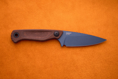 A Benchmade Dacian with a brown Micarta textured handle and a matte, dark CPM-Magnacut steel blade rests on an orange surface.