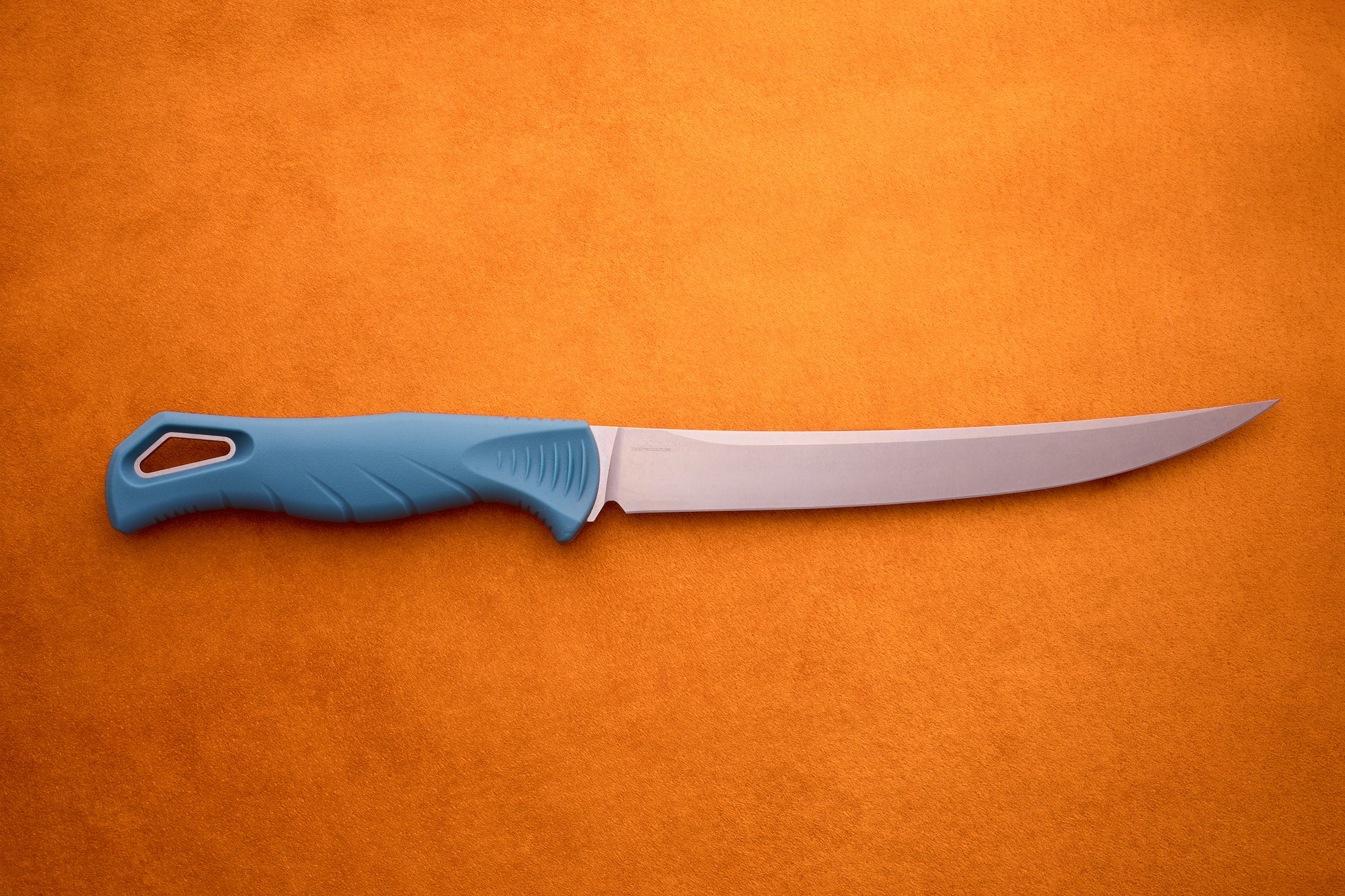 A Benchmade Fishcrafter with a long, thin blade and blue handle lies on an orange surface, making it ideal for precise filleting tasks.