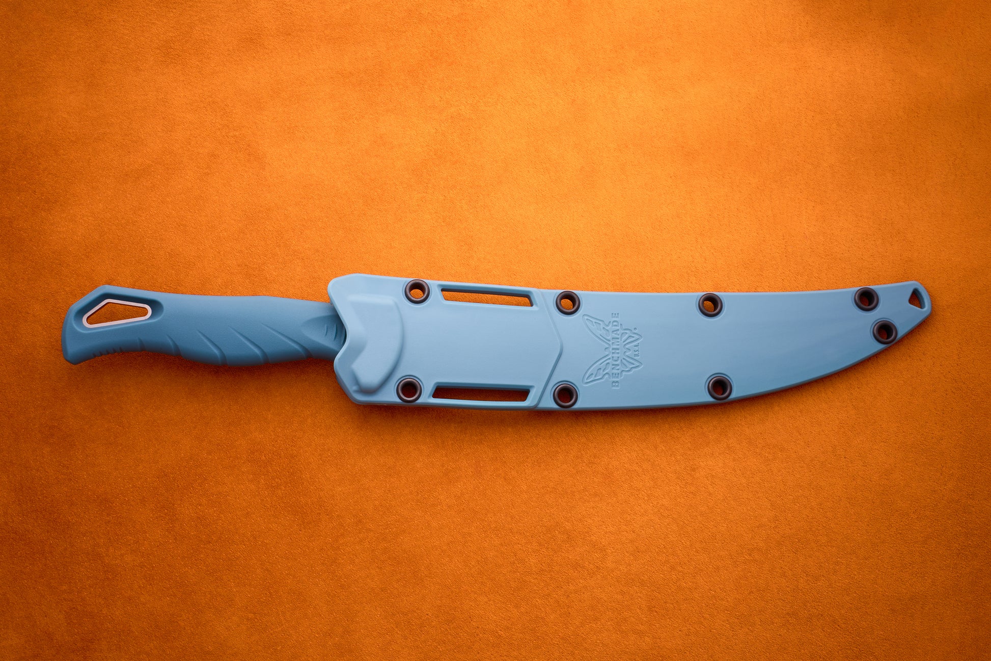 A blue Benchmade Fishcrafter knife with a matching blue sheath lies on an orange textured surface, secured by black rivets, with the Benchmade logo etched near the blade—a sleek tool ideal for precise filleting.