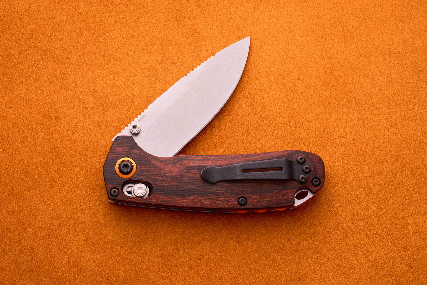 Benchmade North Fork folding pocket knife with a partially open CPM-S30V stainless steel blade and wooden handle, placed on an orange textured surface.