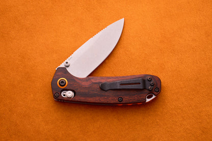 Benchmade North Fork folding pocket knife with a partially open CPM-S30V stainless steel blade and wooden handle, placed on an orange textured surface.