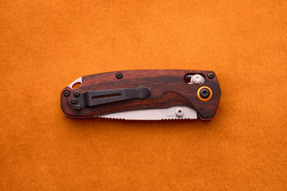 A Benchmade North Fork folding pocket knife with a wooden handle and a partially visible CPM-S30V blade lies closed on an orange suede surface.