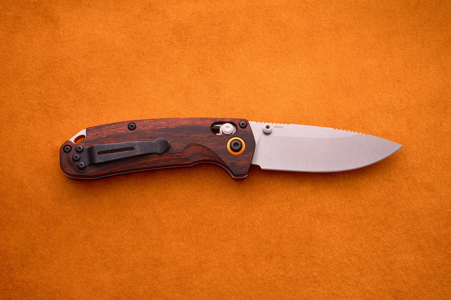 A Benchmade North Fork folding pocket knife with a wooden handle and a partially open CPM-S30V blade lies on an orange suede surface, showcasing its finely crafted design.