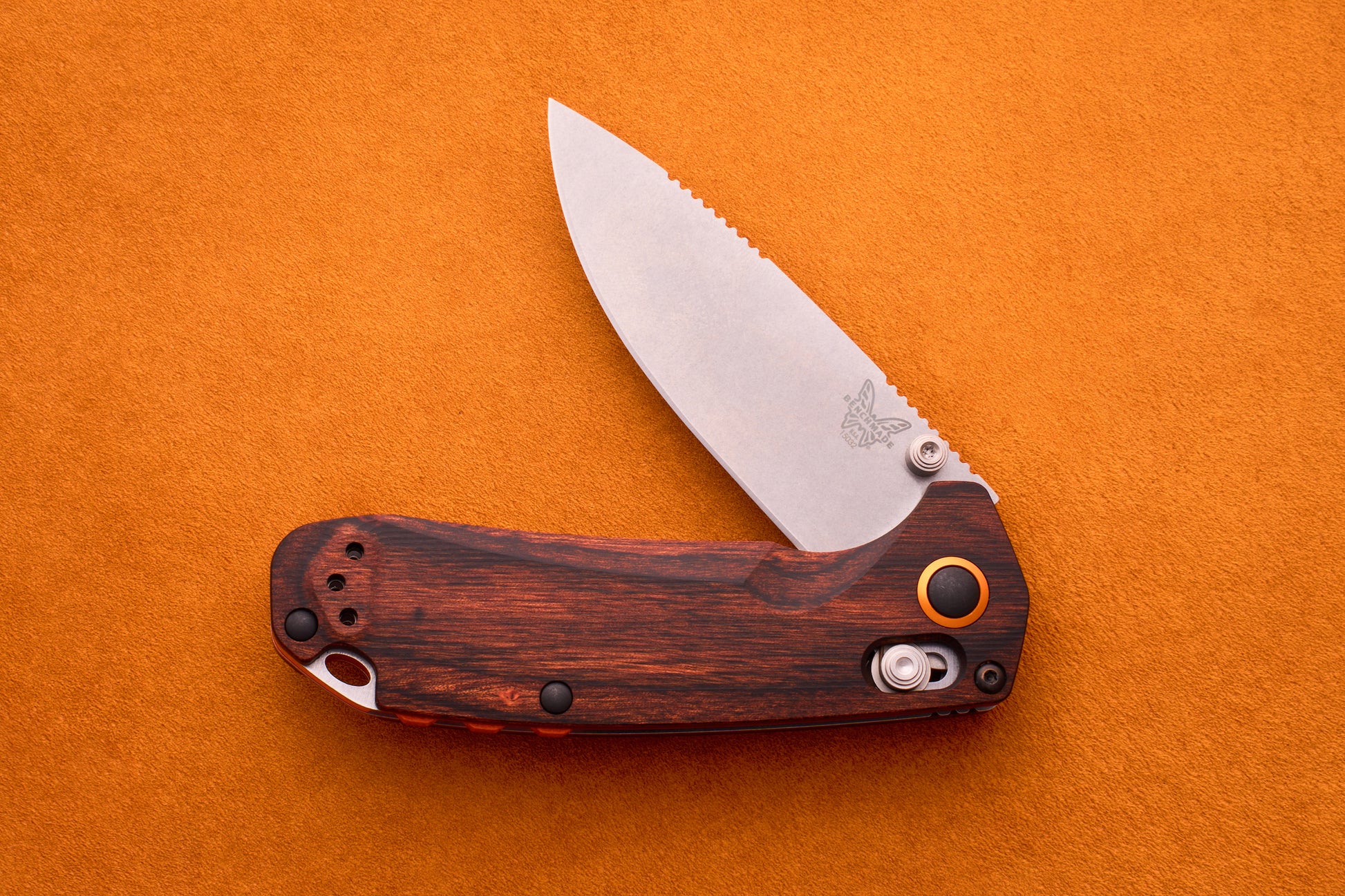 A Benchmade North Fork folding pocket knife featuring a wood-patterned handle and a partially open silver CPM-S30V blade, displayed on an orange textured background.