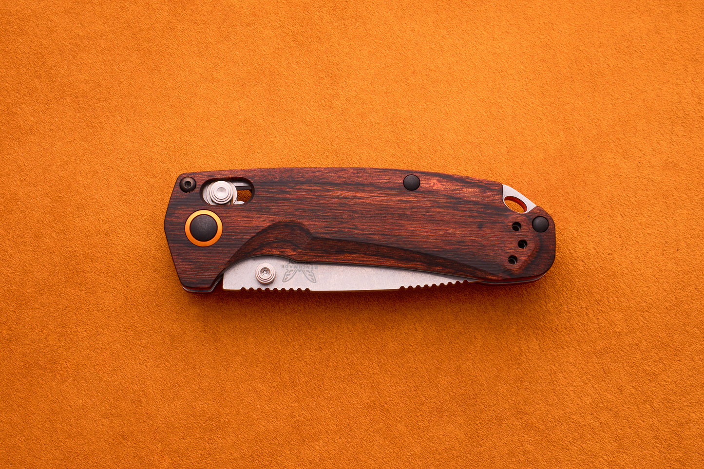 A Benchmade North Fork folding pocket knife with a wooden handle and a partially visible serrated CPM-S30V blade rests on an orange textured surface.