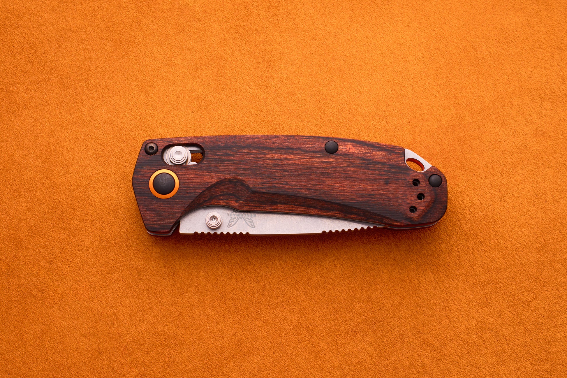 A Benchmade North Fork folding pocket knife with a wooden handle and a partially visible serrated CPM-S30V blade rests on an orange textured surface.