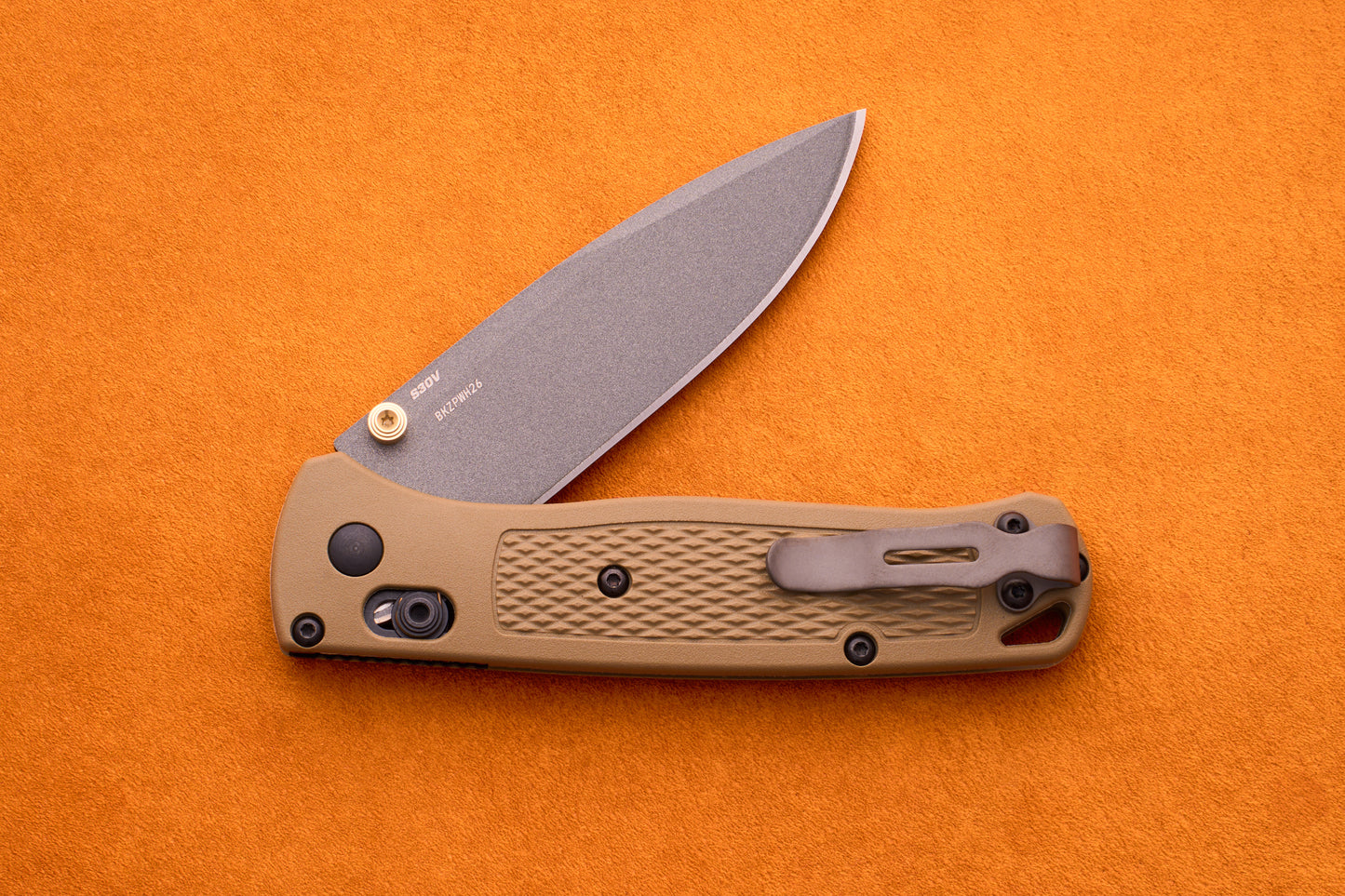 A tan-handled Benchmade Bugout folding pocket knife with a partially open blade is displayed on an orange background, highlighting its durable S30V stainless steel construction—an ideal choice for any outdoor adventure knife enthusiast.