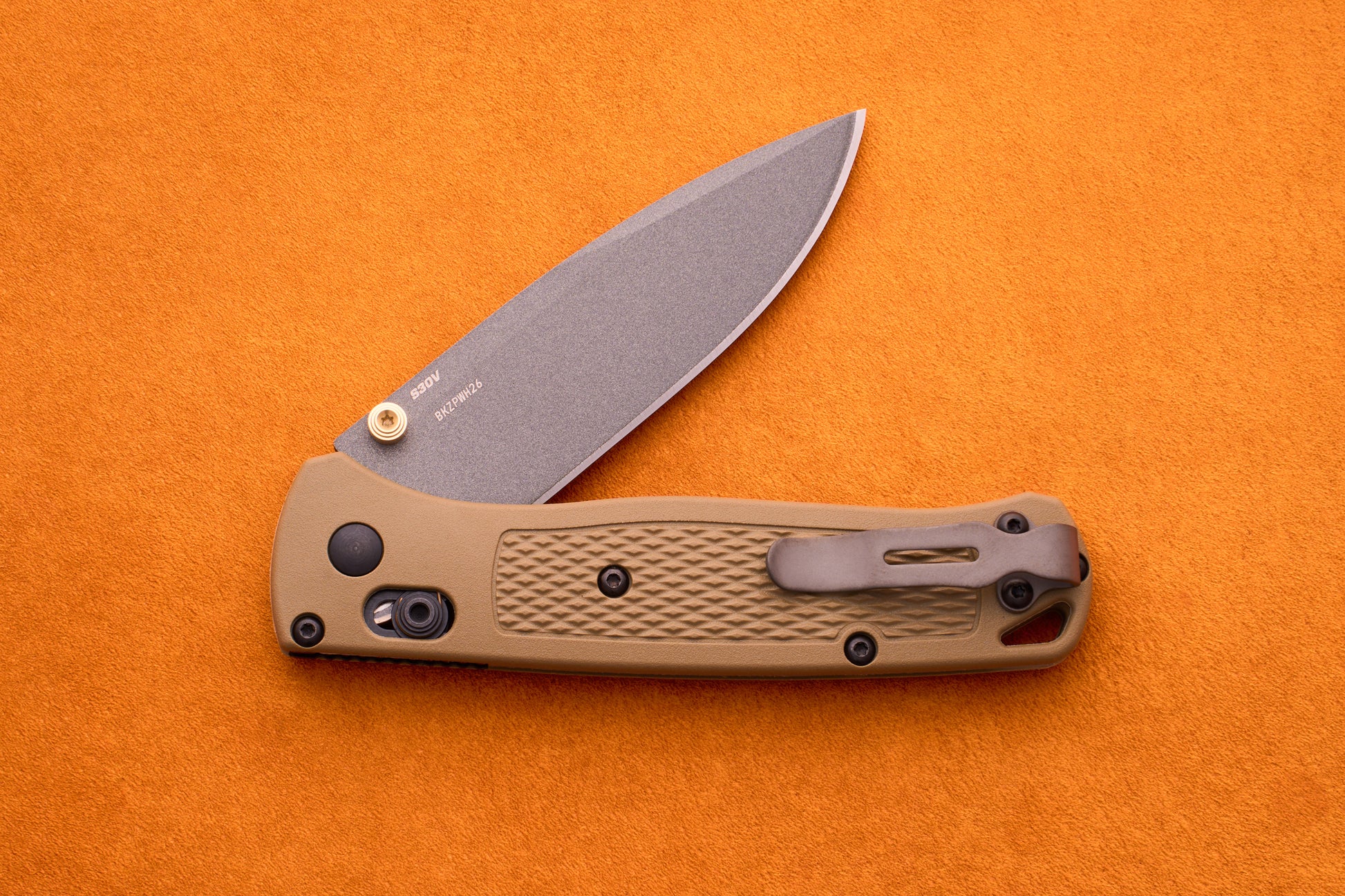 A tan-handled Benchmade Bugout folding pocket knife with a partially open blade is displayed on an orange background, highlighting its durable S30V stainless steel construction—an ideal choice for any outdoor adventure knife enthusiast.