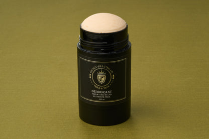 A black cylindrical Crown Shaving Co. Aluminum-Free Deodorant stick with a beige top rests on a green surface. The label features the Signature Blend and emphasizes that it is an aluminum-free deodorant.