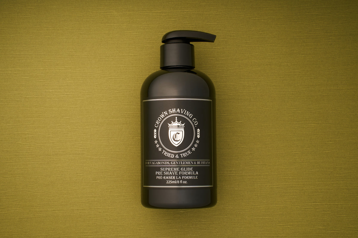 A black bottle of Crown Shaving Co. Preshave 225ml with a pump top rests on a textured green surface. This water-based formula serves as an effective beard lubricant, while the white label displays the company logo and product details.
