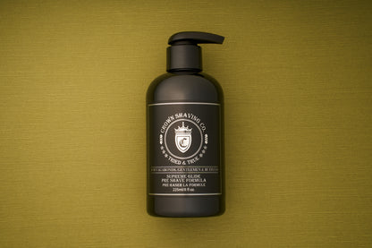 A black bottle of Crown Shaving Co. Preshave 225ml with a pump top rests on a textured green surface. This water-based formula serves as an effective beard lubricant, while the white label displays the company logo and product details.
