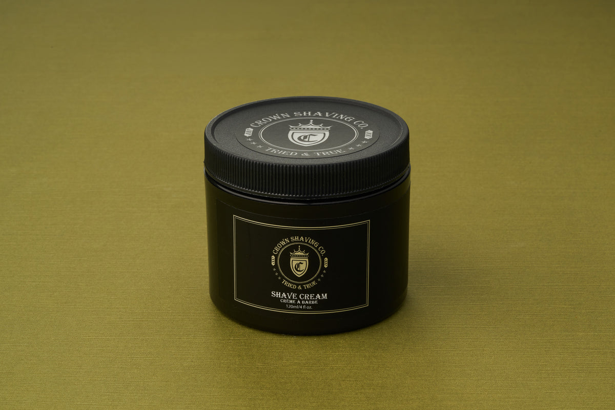 A black tub of Crown Shaving Co. Shave Cream rests on a gold surface. The container, adorned with the brand’s crest and white lettering, emphasizes its sulfate- and paraben-free formula—making it an essential for those in search of a premium Crown Shaving Co. Shave Cream experience.