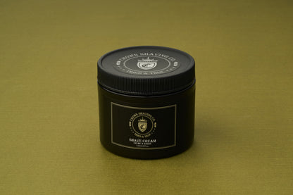A black tub of Crown Shaving Co. Shave Cream rests on a gold surface. The container, adorned with the brand’s crest and white lettering, emphasizes its sulfate- and paraben-free formula—making it an essential for those in search of a premium Crown Shaving Co. Shave Cream experience.